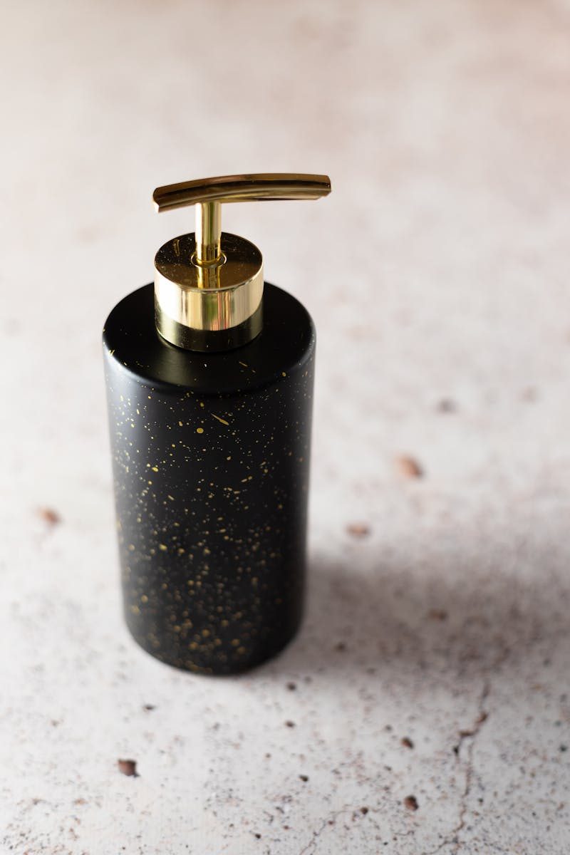 Stylish black soap dispenser with gold pump on a marble surface, ideal for luxurious bathrooms.