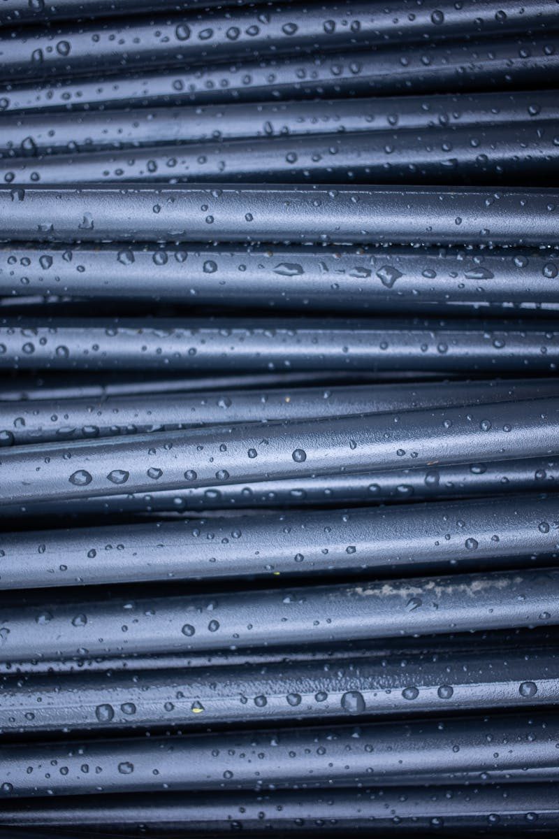 Abstract textured backdrop of full frame dark rubber rods with drops on shiny surface